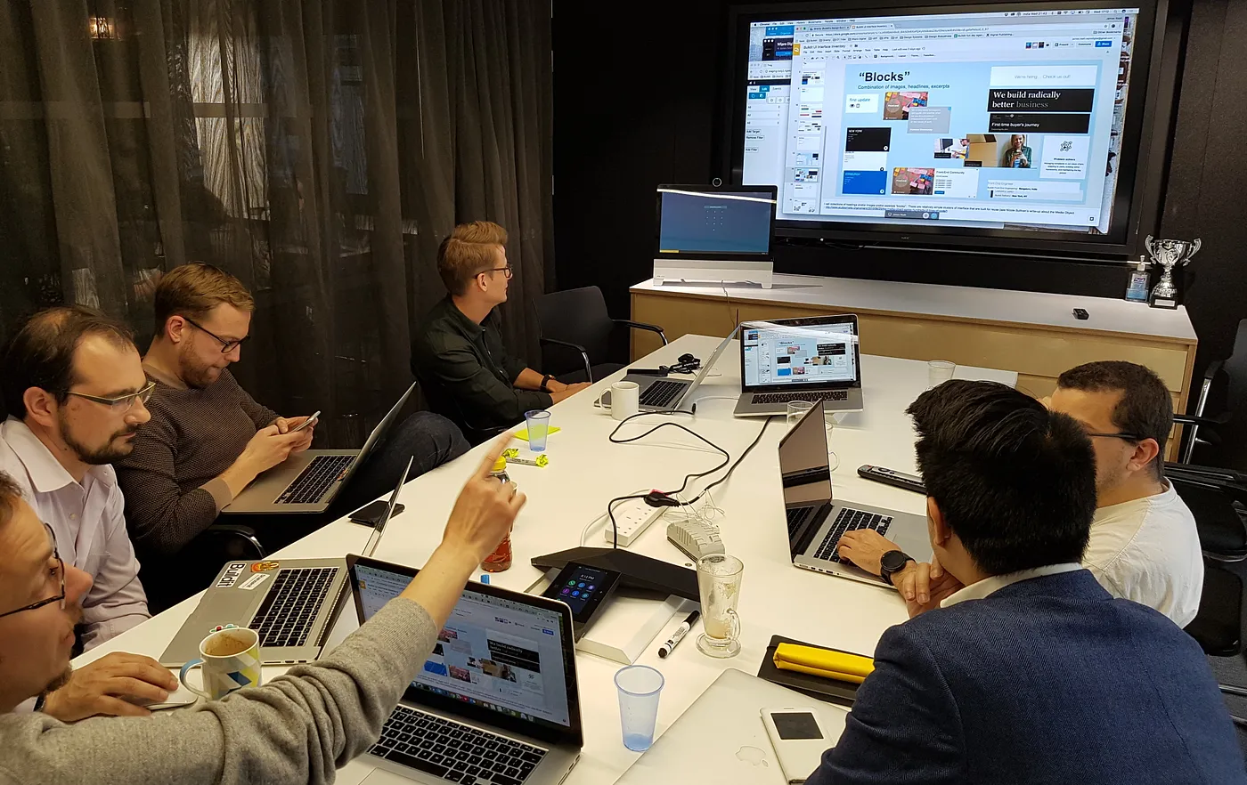 Buildit colleagues in a meeting room discusssing screenshots of UI components that are visible on a large screen.