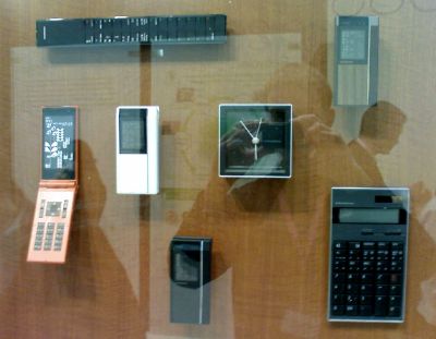 A phone with a sleek, angular design alongside a TV remove, wall clock and calculator that share a similar aethetic