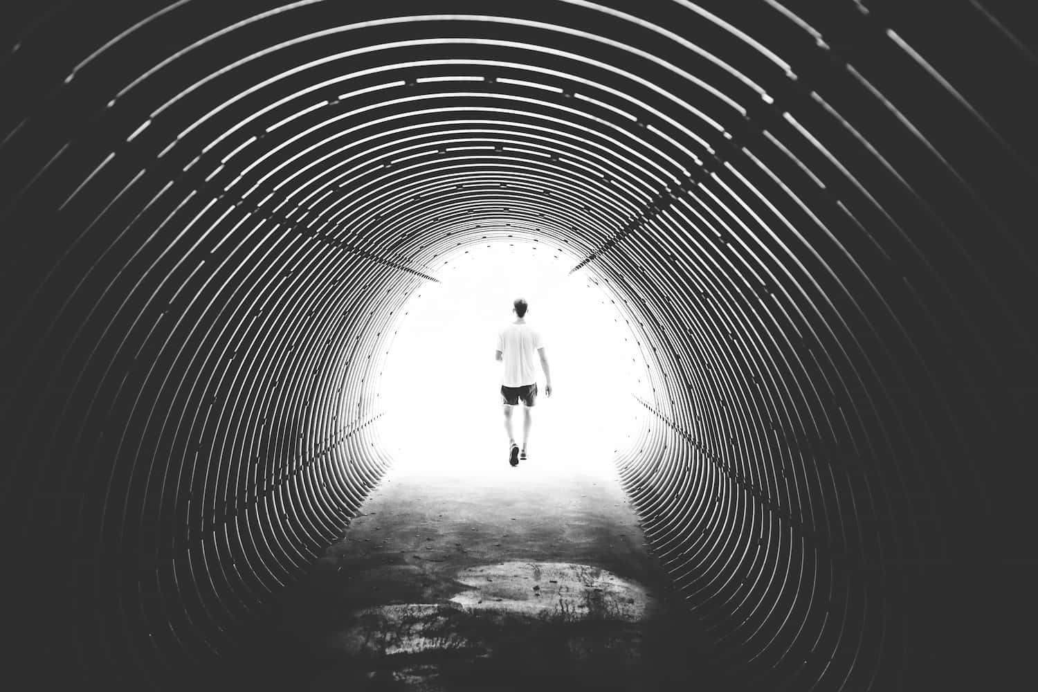 A man walks out of a dark tunnel towards a bright light